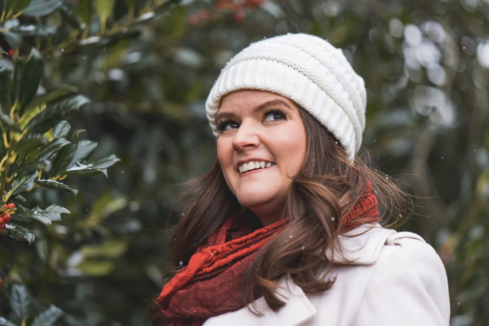 Lindsey in a cream coat and red scarf beside holly in falling snow