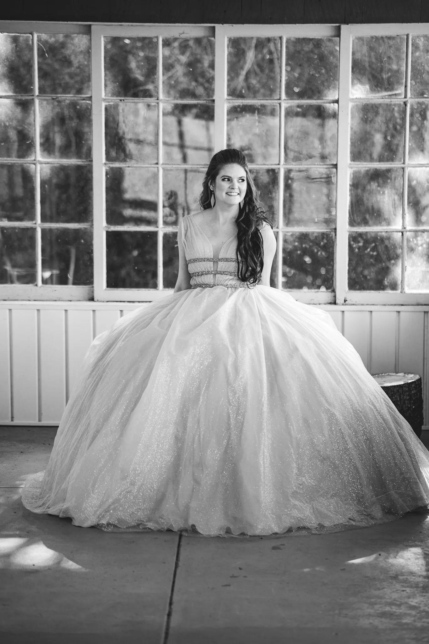 A figure in a pale gown standing alone in the light of tall windows